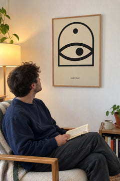 Man reading in an armchair, looking up at the Look Closer print on his living room wall