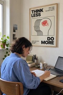 Woman writing at her desk under the Think Less print
