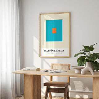 Wall office art of blue and orange squares above a wooden desk with books and a plant