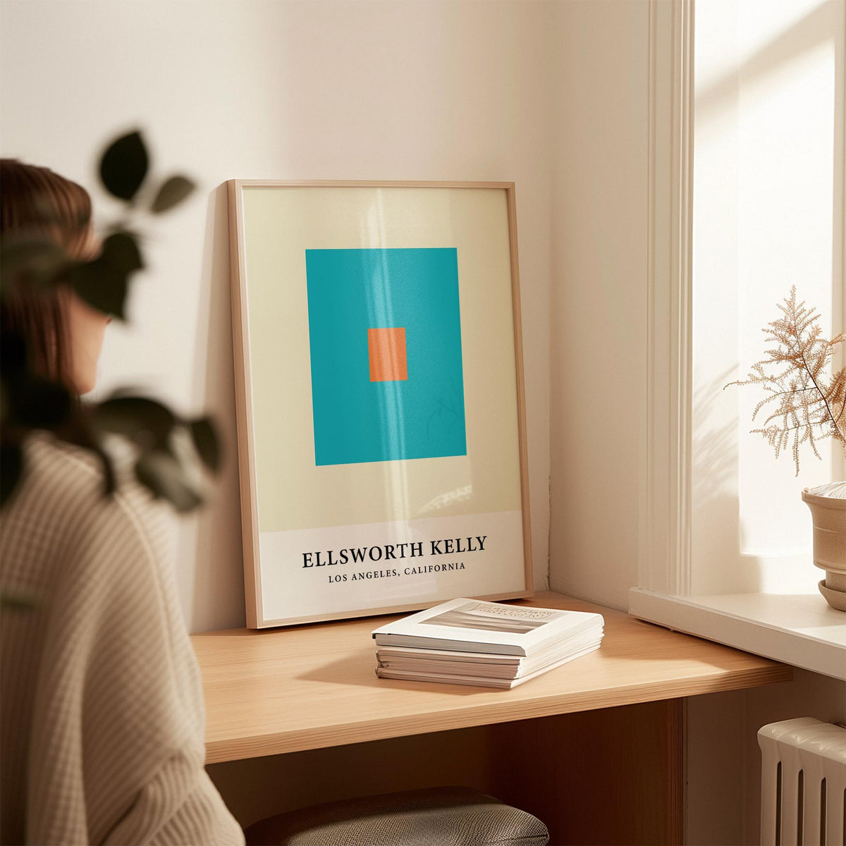 Print leaning on a desk of orange and blue squares with a stack of books nearby in a warmly lit room