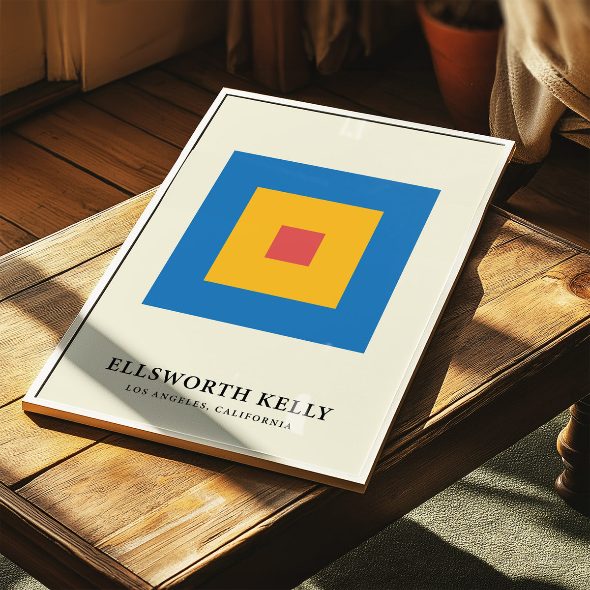Minimalist Art print with concentric red yellow and blue blocks lying on a wooden table near a plant pot
