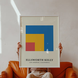 Framed print of nested blue yellow and red squares held by a person sitting on an orange sofa
