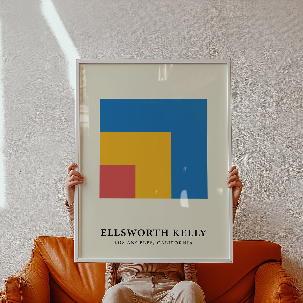 Framed print of nested blue yellow and red squares held by a person sitting on an orange sofa
