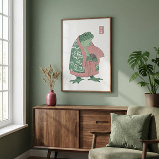 Frog Art Print hanging above a wooden sideboard with a red vase and plant in a green walled room