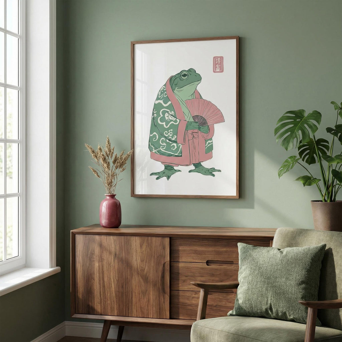 Frog Art Print hanging above a wooden sideboard with a red vase and plant in a green walled room