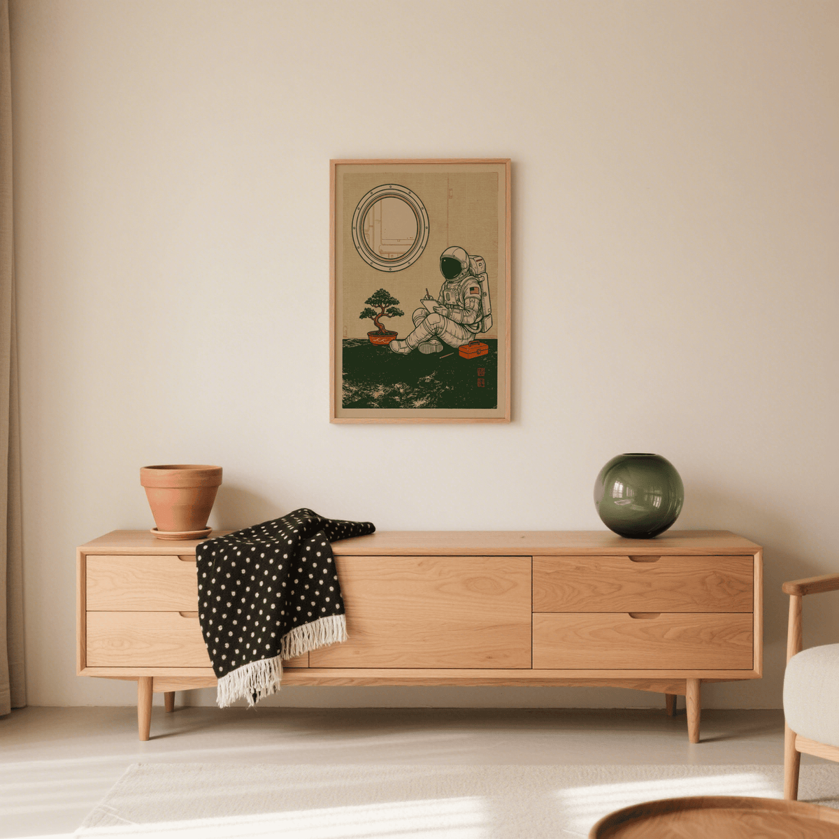 Framed Astronaut Art Print of a sitting astronaut sketch in black and beige over a sideboard with plant pot and vase