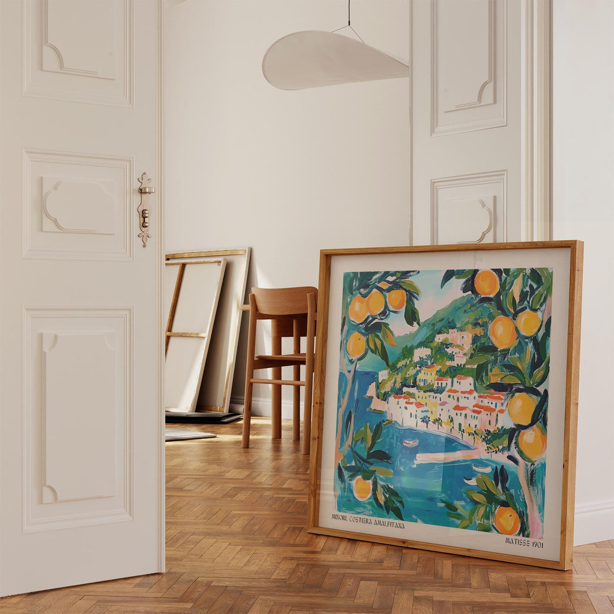 Print leaning on a parquet floor shows Amalfi wall art of a coastal village with oranges and blue sea