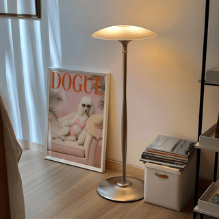 Pink Poodle Print leaning on the floor by a standing lamp and stack of magazines in a soft lit room