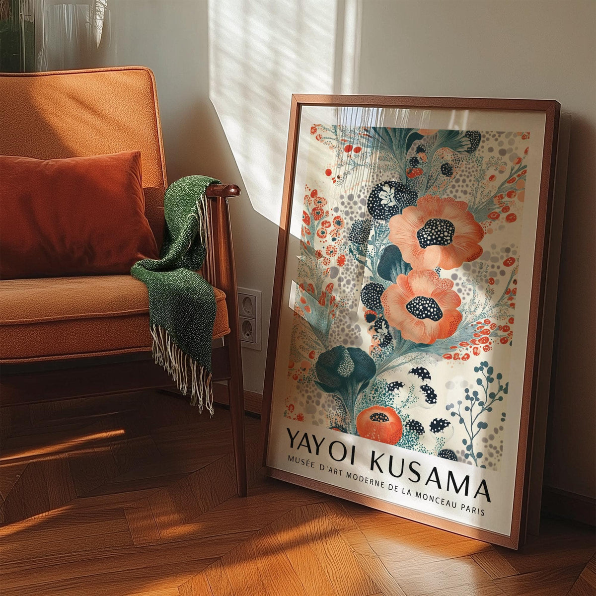 Floral poster wall art with orange and teal flower blooms leaning on floor next to an orange armchair