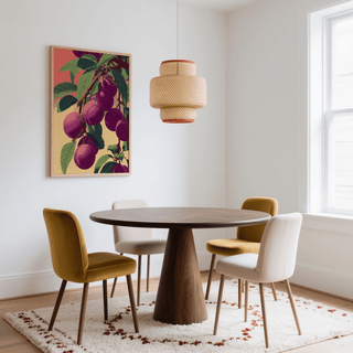 Print on a wall in a dining room showing plums on a branch with green leaves and a red and beige background above a round wooden table