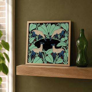 Print leaning on a wooden shelf of colourful animal wall art with spotted deer and green foliage beside a green glass bottle