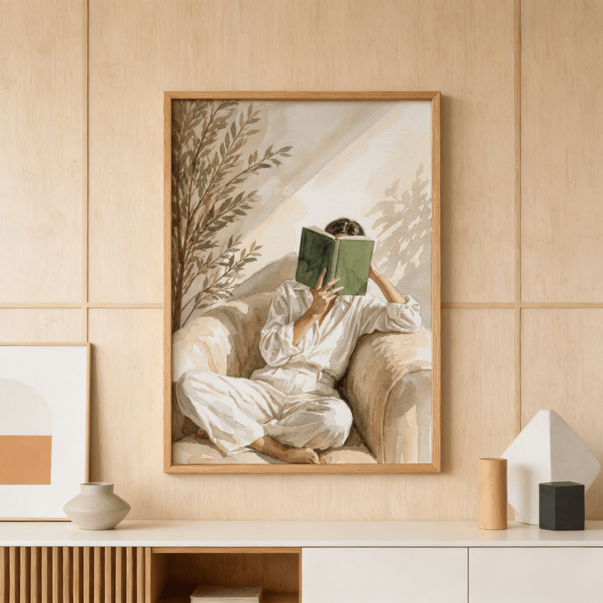 Neutral Woman Reading Art Print framed on a wood panel wall above a cabinet with vases