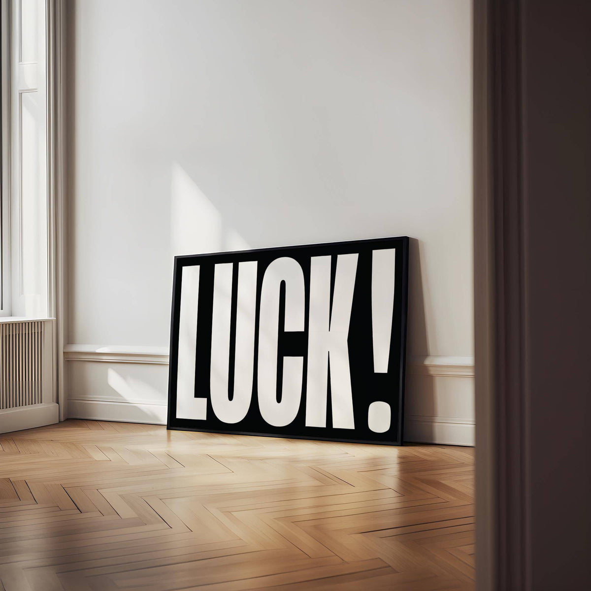Print leaning on floor featuring the word luck in bold white letters on black background with wooden herringbone floor