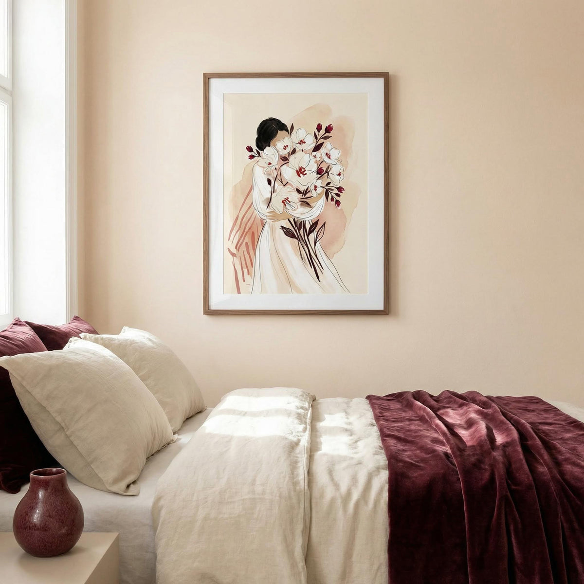 Woman Holding Flowers print with soft watercolour tones above a bed with cream cushions and a dark red throw