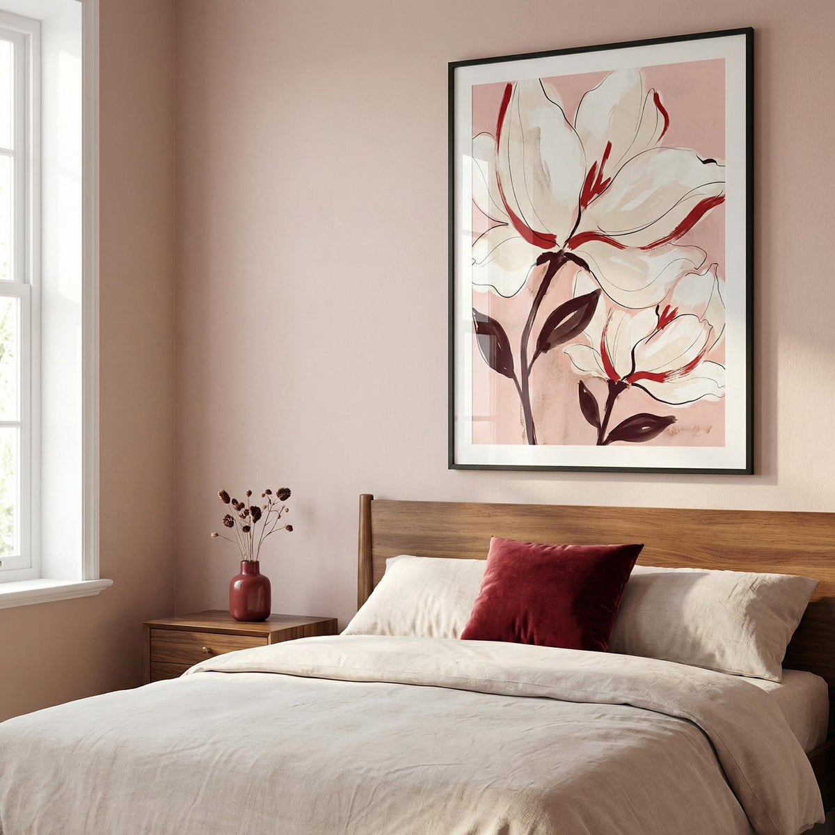 Flower print leaning on a soft pink wall above a wooden bed with a red throw cushion in a bedroom