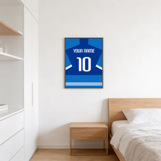 Print of a football shirt poster in two-tone blue with white sleeve stripes above a wooden bedside table in a bedroom