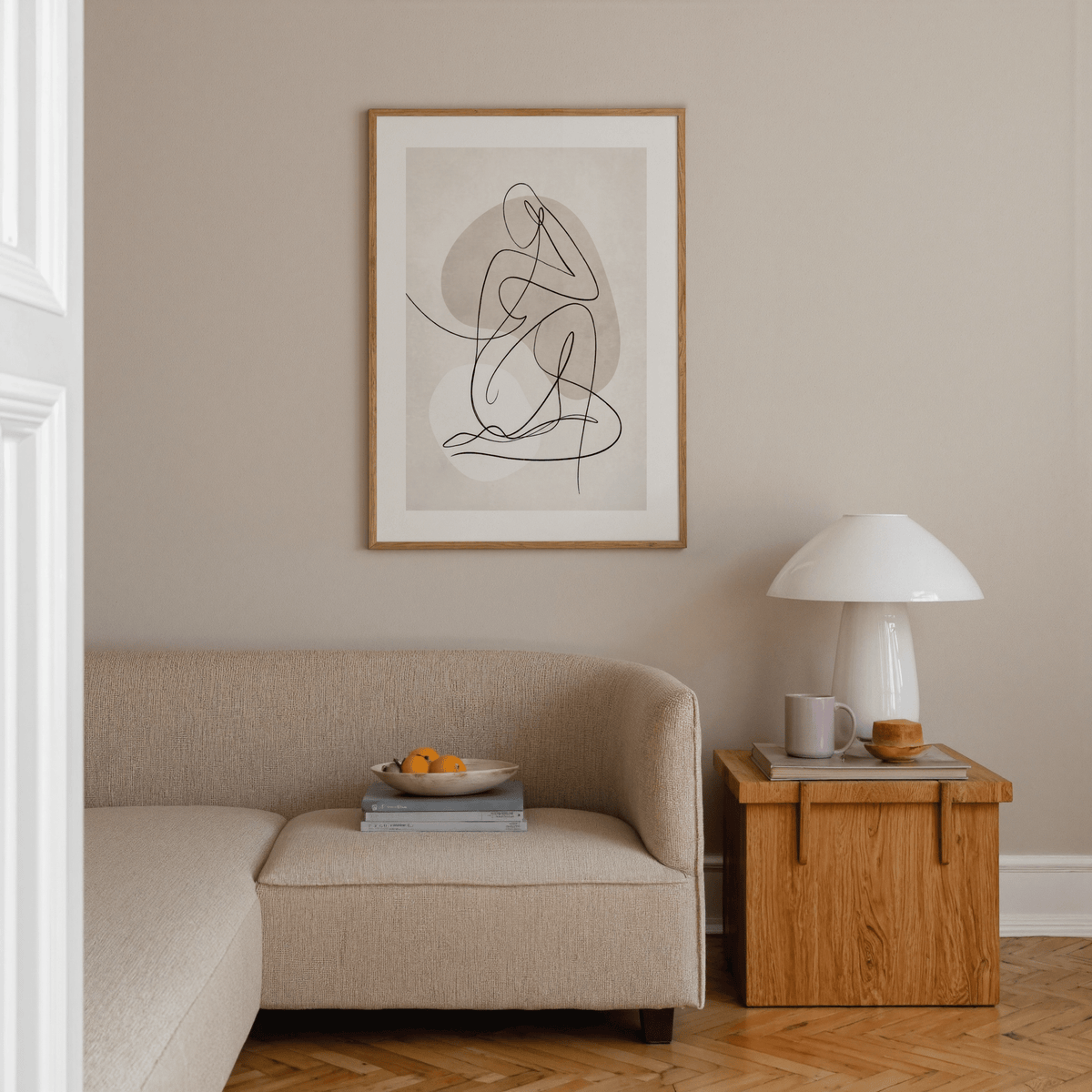 Abstract line art poster of a seated figure in beige and white above a corner sofa with a wooden side table and lamp