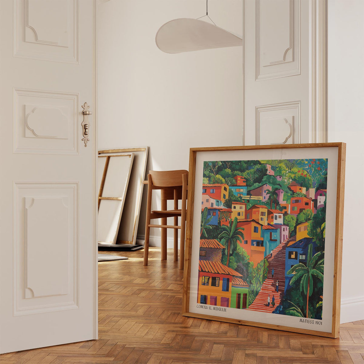 Comuna 13 art print leaning on wooden parquet floor near a chair and stacked empty frames in a bright room