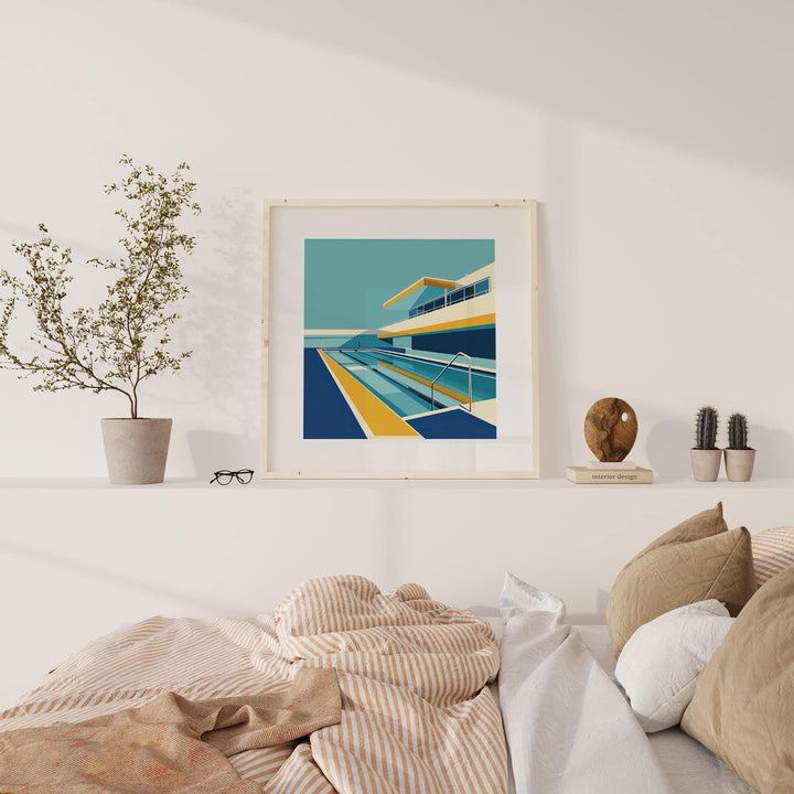 Framed Poolside Art print of a modern poolside scene in blue yellow and cream tones on a shelf with plants and books