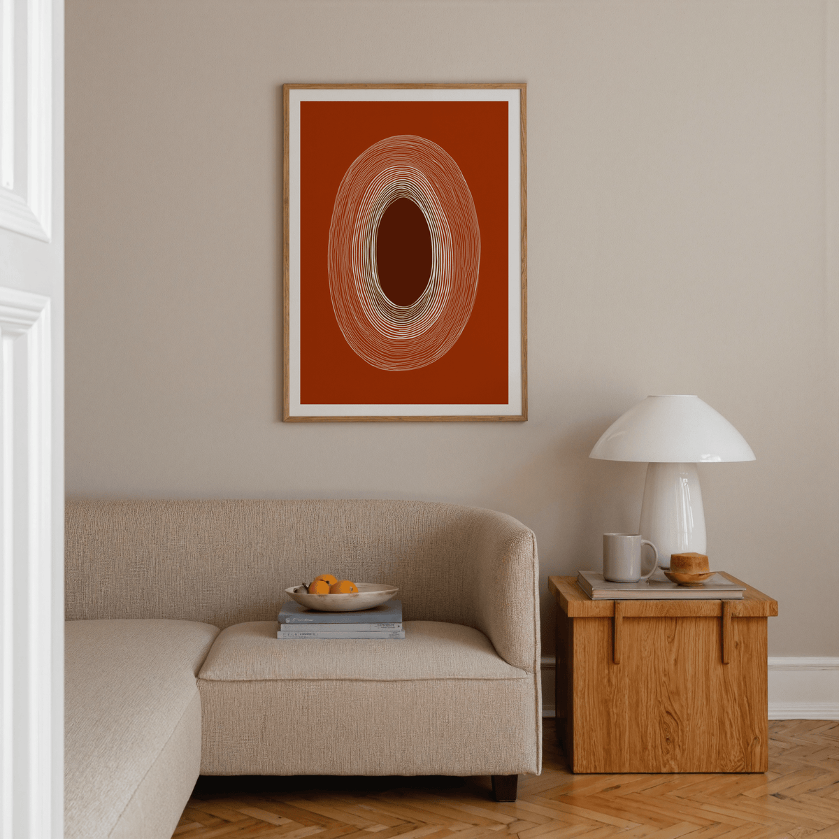 Abstract Line Drawing Poster on a beige wall above a sofa with concentric oval lines in rust and white with an oak side table beside it