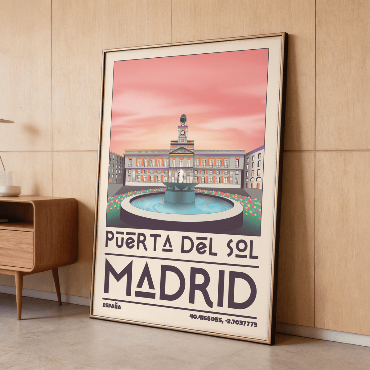 Print leaning on a shelf of Madrid landmark art print showing Puerta del Sol plaza with a pink sky in a wood room