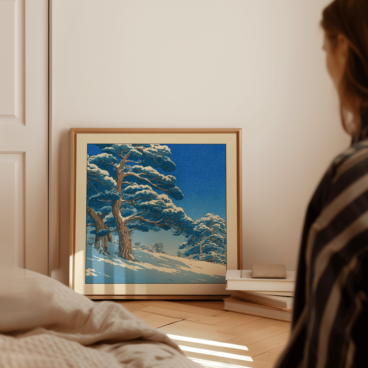 Hasui Kawase Snowy Pines Art Print leaning on a wooden floor beside books in a warmly lit room
