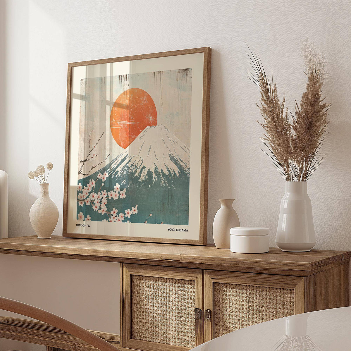 Square print of Mount Fuji with red sun and pink cherry blossoms leaning on a wooden sideboard with white vases