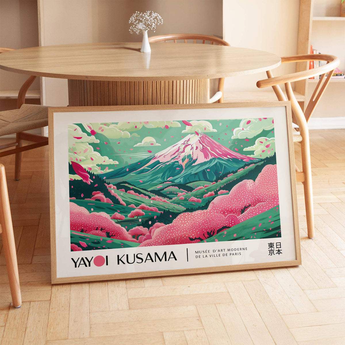 Print leaning on floor of cherry blossom art with pink and green hills beside wooden table and chairs