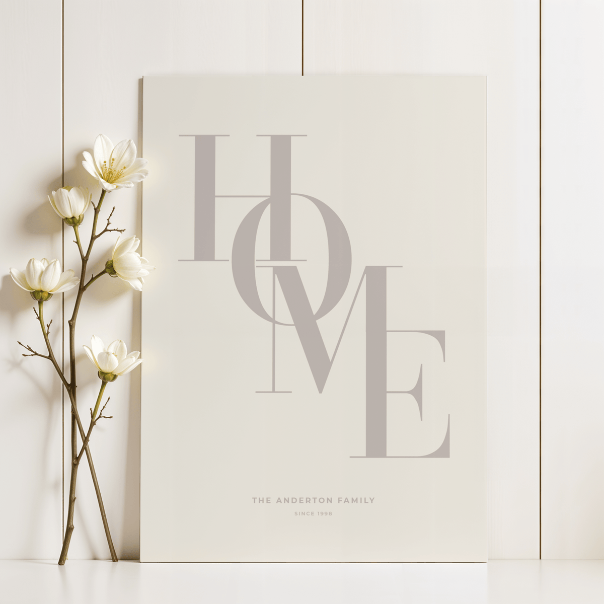 Close-up of Home Beige Personal Print leaning on a white wooden wall next to white flowers