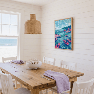 Sailboats wall art in a coastal dining room with wooden table and white chairs