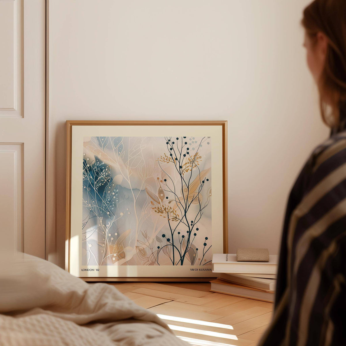 Neutral prints leaning print of abstract botanical illustration in soft blue and beige tones beside books