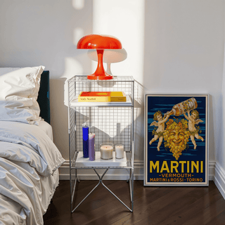 Print leaning on the floor of Vintage Vermouth poster with yellow text beside white and orange bedside table