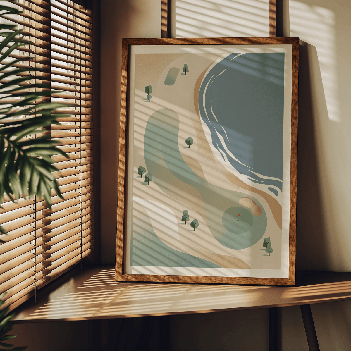 Print leaning on a shelf of minimalist coastal golf course art print with sea blues and sandy colours near plant