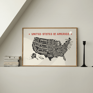 Print of Us Map Poster with minimalist black and red typography leaning on a white shelf next to a black candlestick