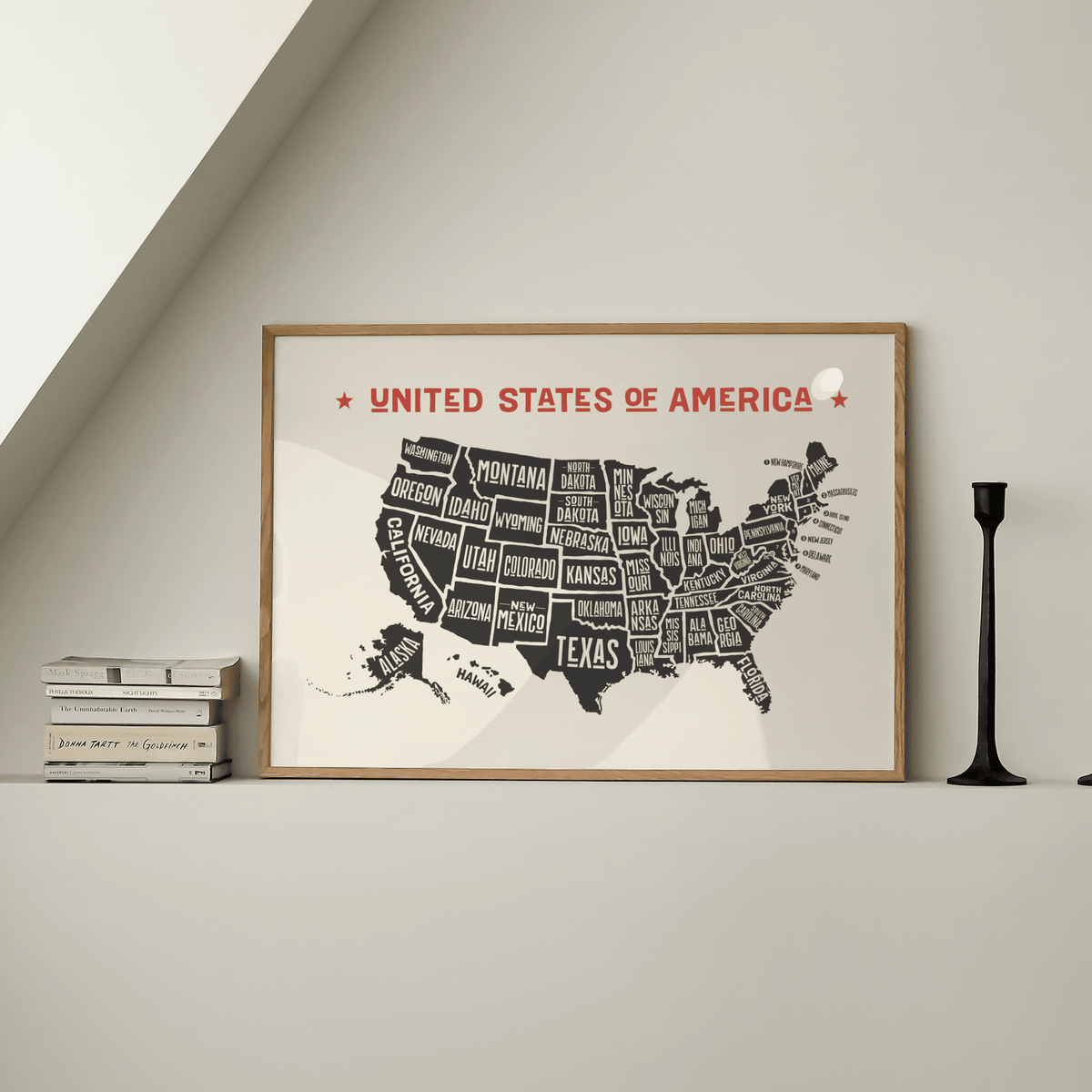Print of Us Map Poster with minimalist black and red typography leaning on a white shelf next to a black candlestick