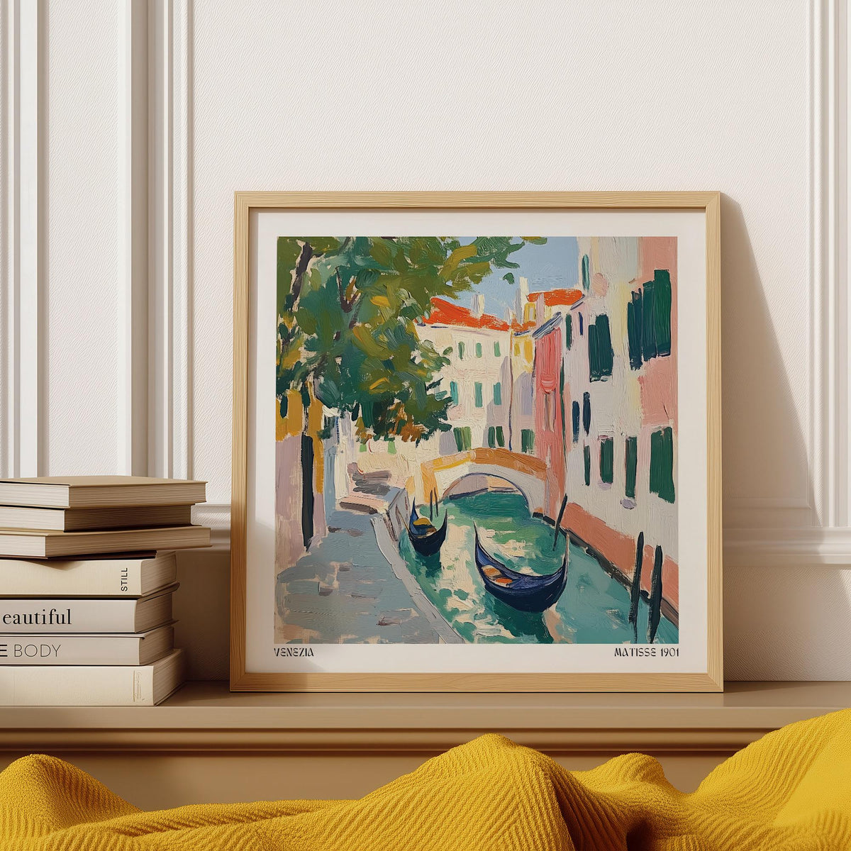 Framed Venice wall art of two gondolas on a canal with warm colours on a shelf with books