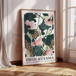 Framed wall art with pink flowers and dark green leaves leaning against a wall with sunlight