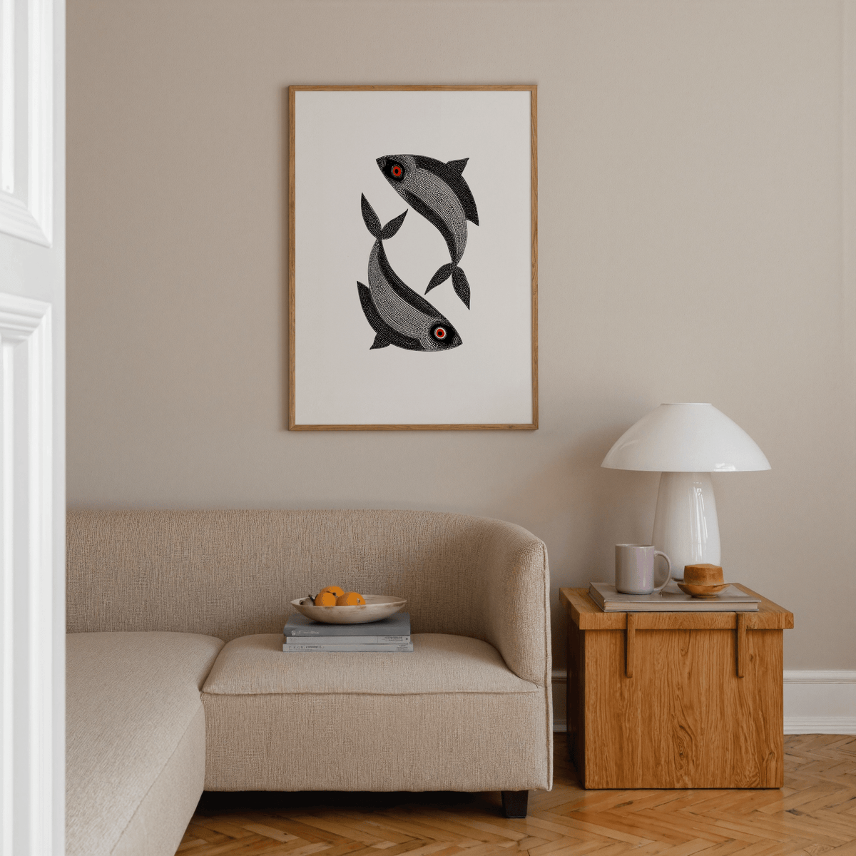 Framed Madhubani Fish wall art with two black fish with red eyes above a beige sofa and wooden side table