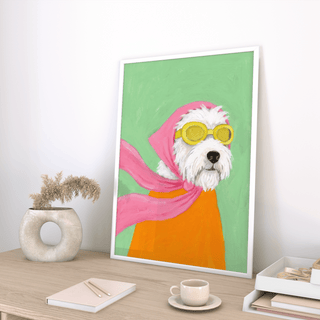 Print leaning on a shelf of dog with aviator goggles and pink scarf in green and orange colours with a vase nearby