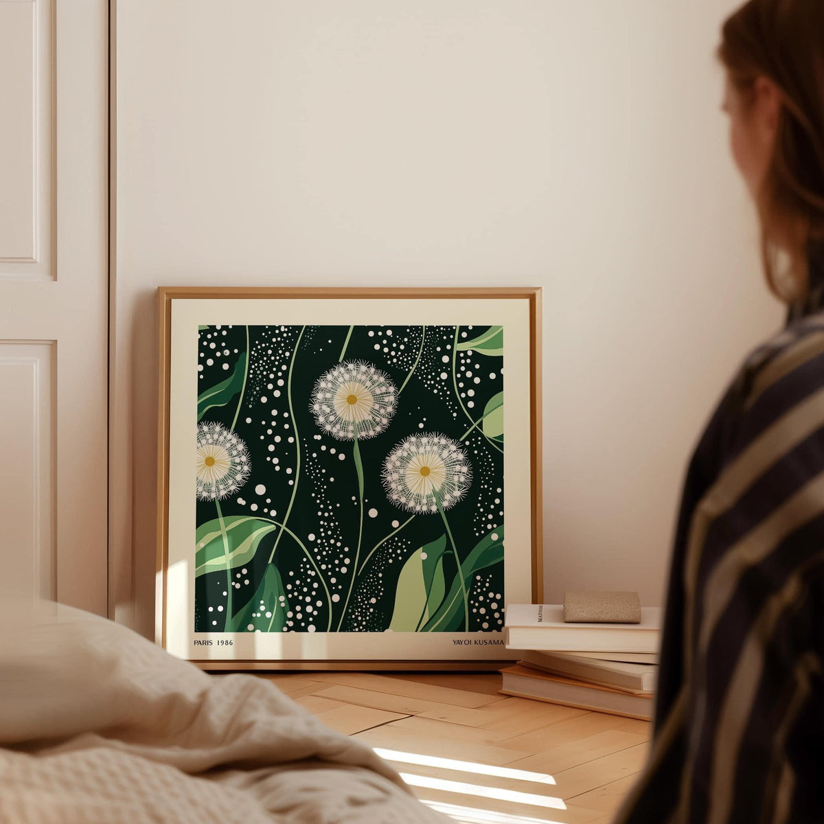 Green wall decor print of dandelion seed heads leaning on a wooden floor with books nearby