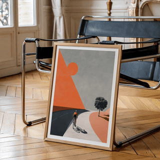 Print leaning on a floor next to a black metal chair showing a cyclist in minimalist colours of orange and grey