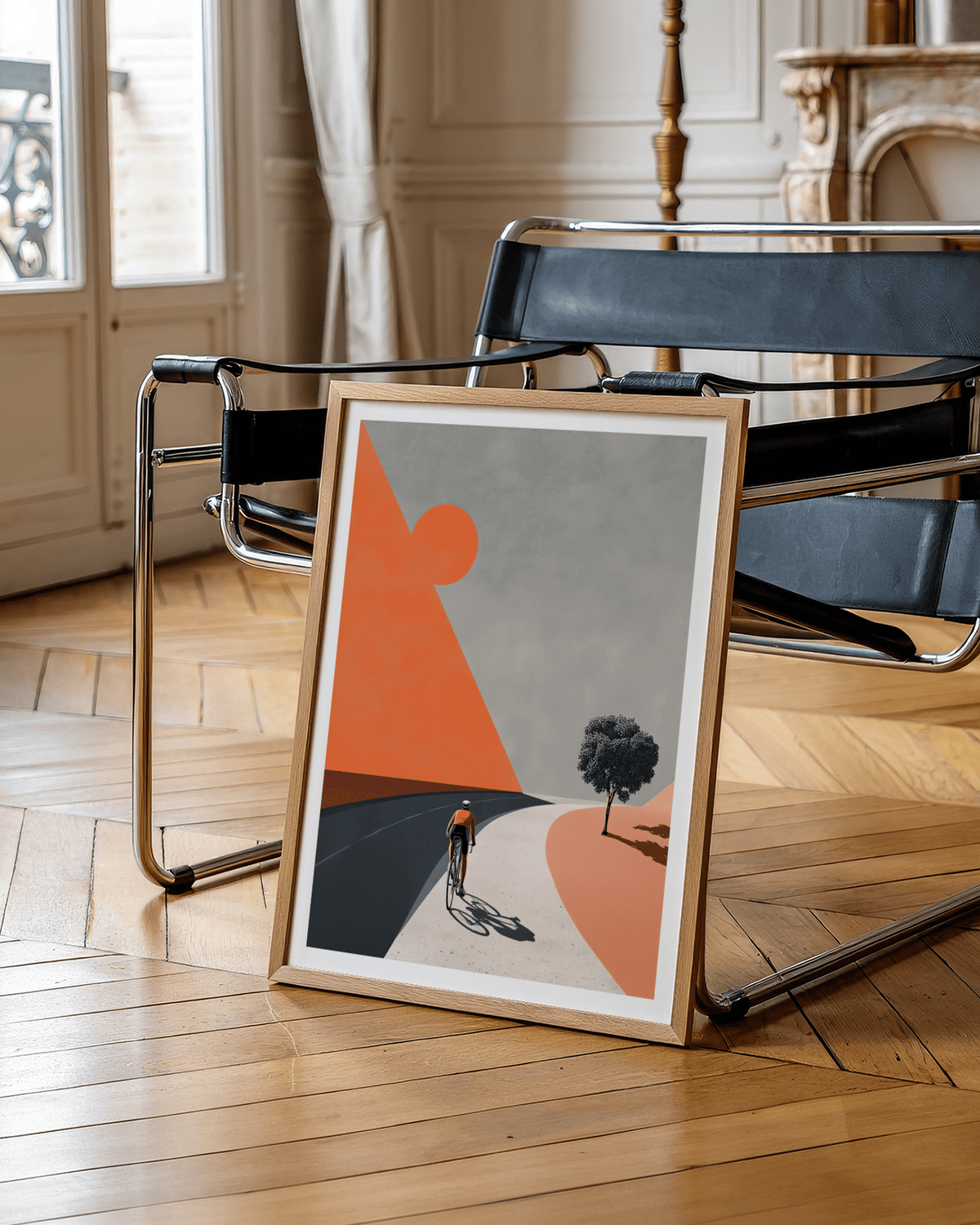 Print leaning on a floor next to a black metal chair showing a cyclist in minimalist colours of orange and grey