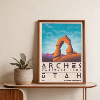 Framed print of Utah wall art featuring Delicate Arch in orange and purple tones on a table with a plant