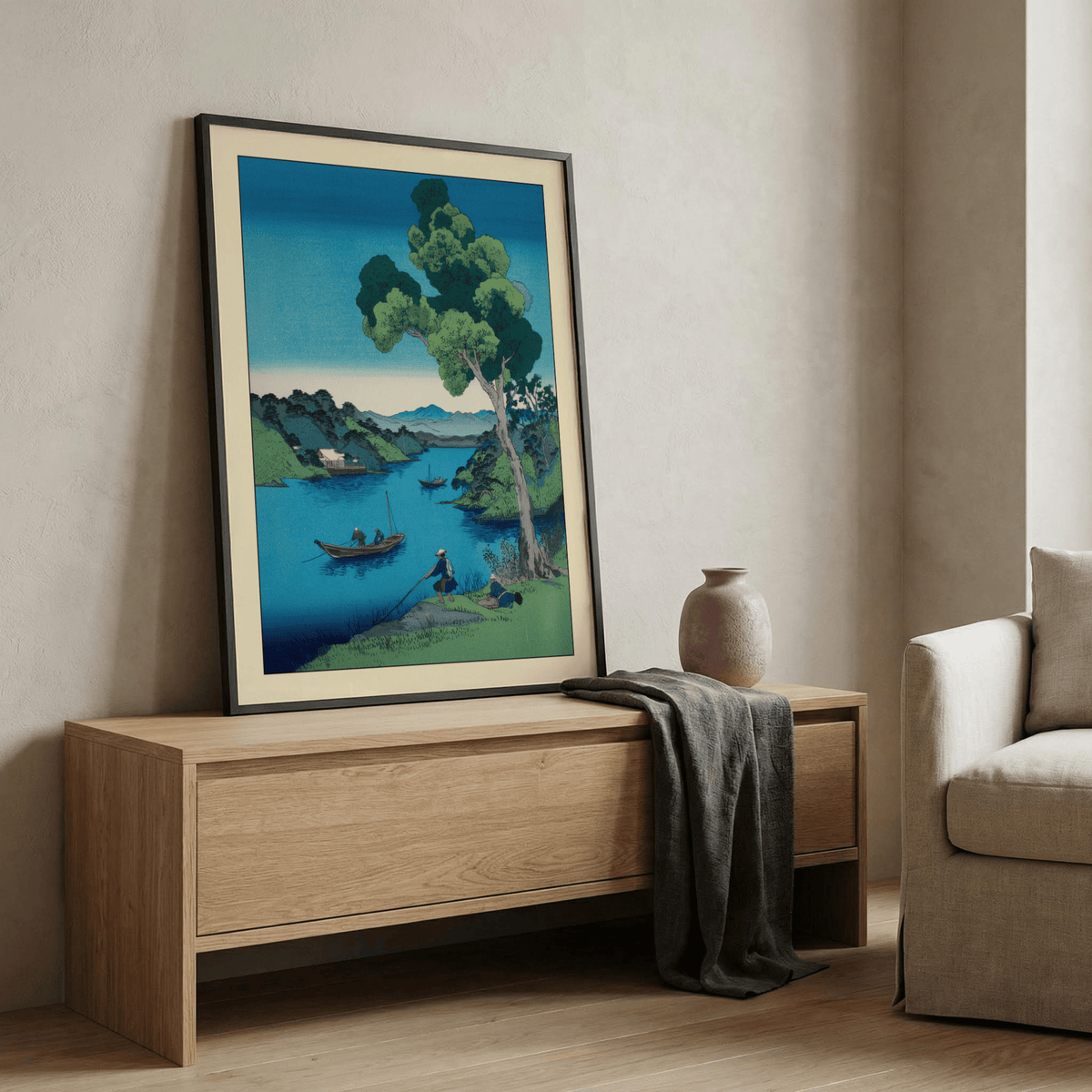 Print leaning on a shelf showing a blue and green Japanese woodblock river landscape with a fishing boat and tree with pottery vase nearby