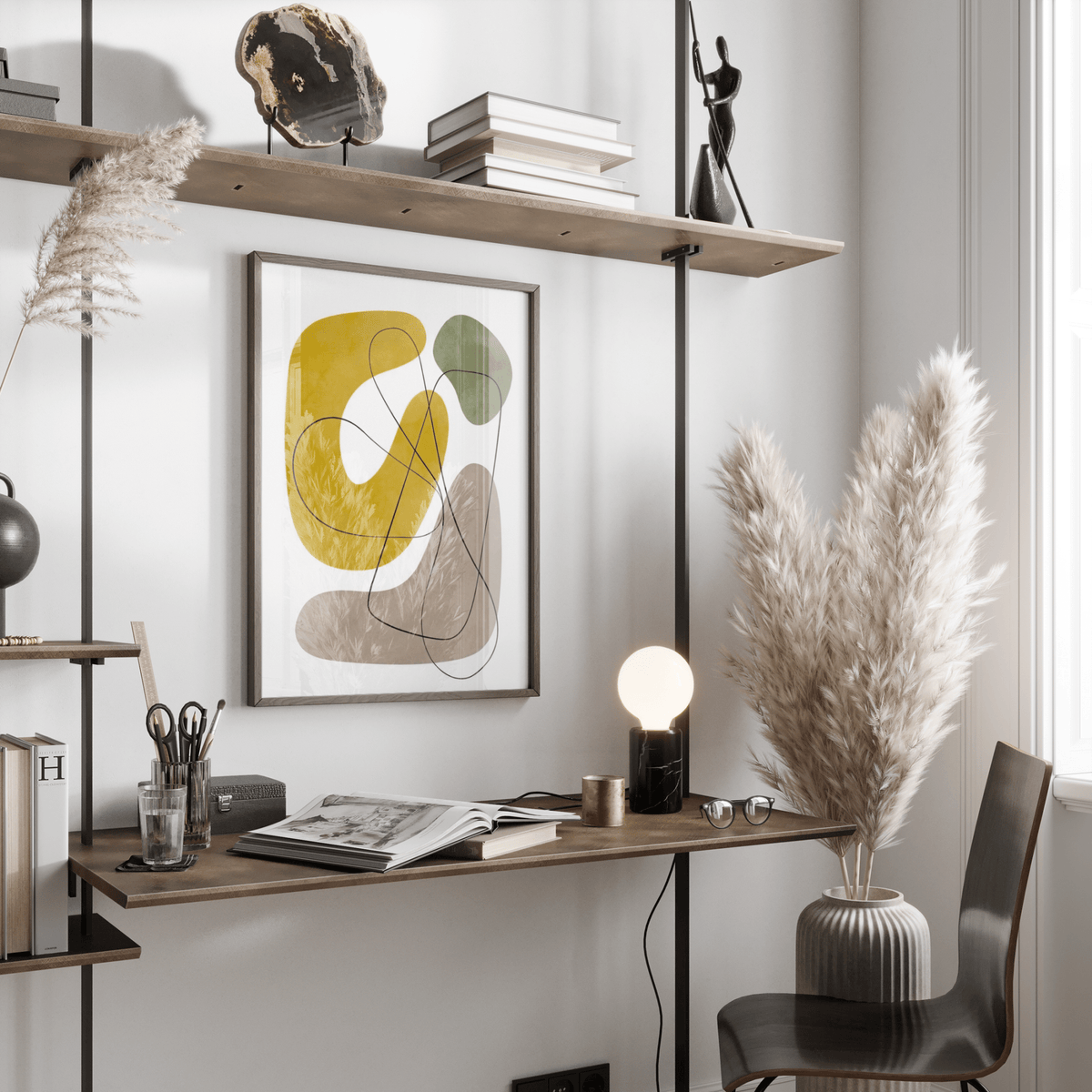 Abstract wall print with yellow, green and grey shapes above a desk with a lamp and glasses in a bright room
