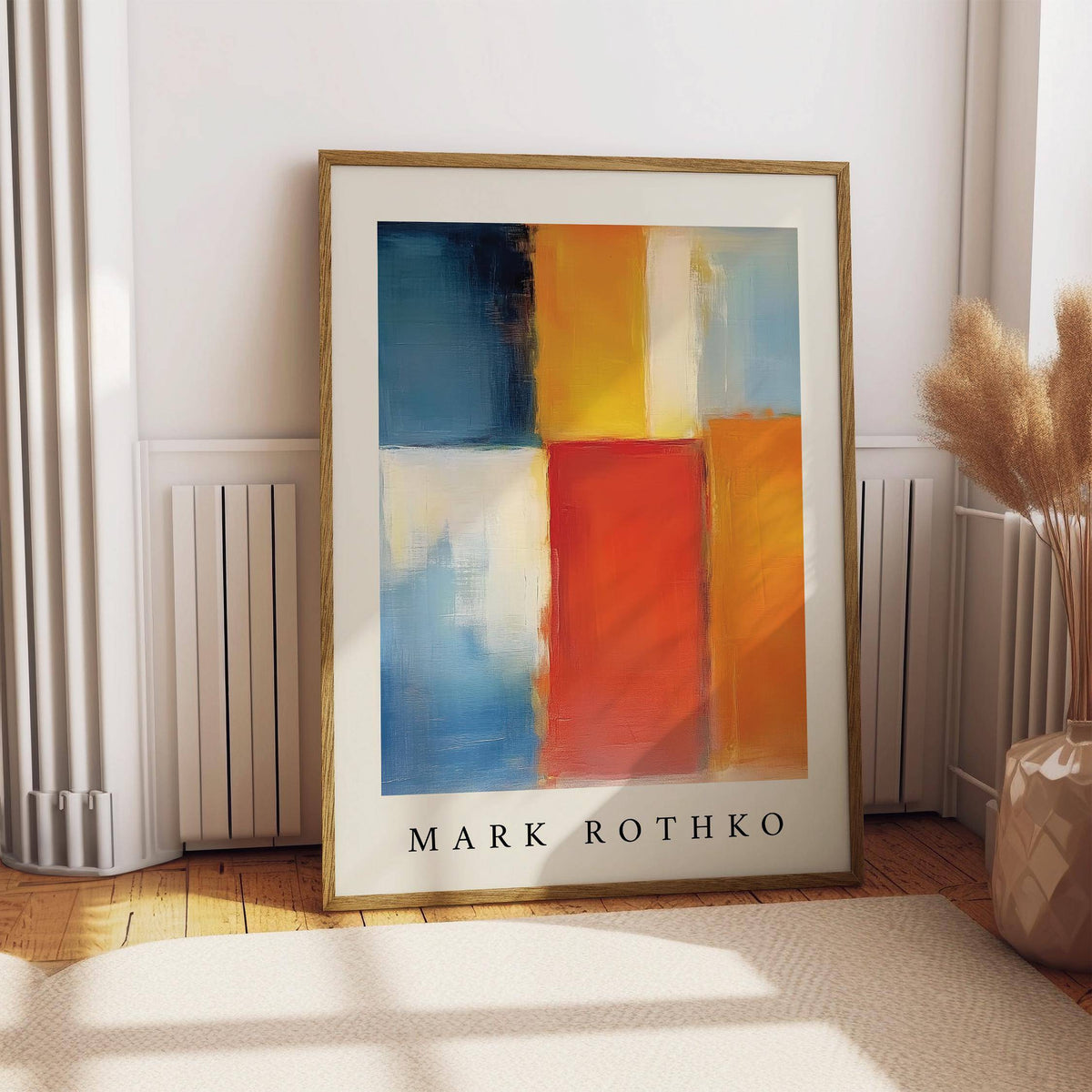 Print leaning on a floor showing an abstract colour block painting with orange red and yellow beside a beige vase with pampas grass