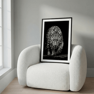 Framed Black Leopard wall art leaning on a white modern armchair in natural light