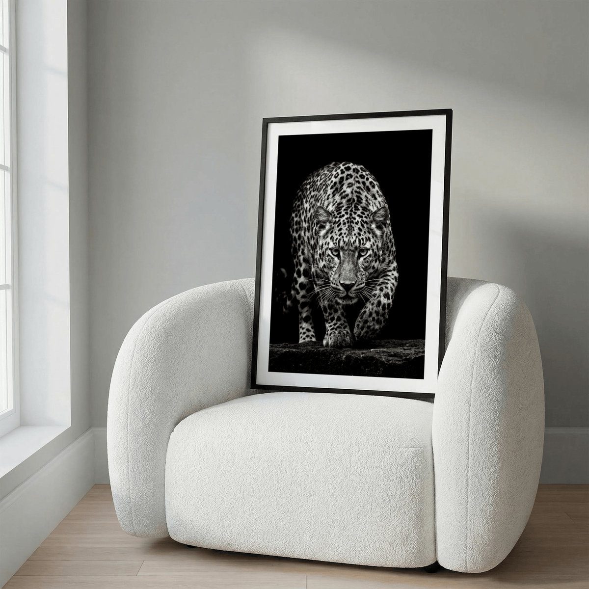 Framed Black Leopard wall art leaning on a white modern armchair in natural light