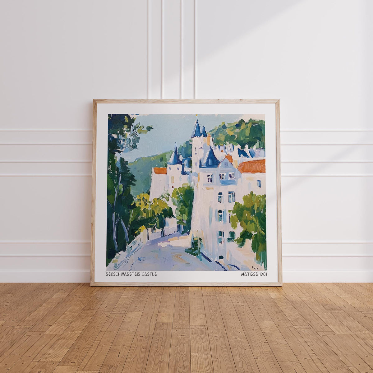 Framed print of medieval castle art with blue rooftops and green trees leaning on a wooden floor
