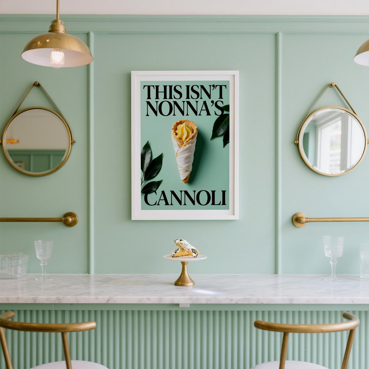Italian Kitchen Art framed print with a wrapped cannoli pastry on a mint green wall above a marble counter with a cannoli on a cake stand